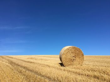 Hay bales on field against clear blue sky