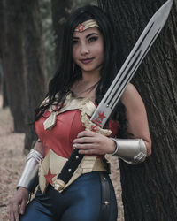 Portrait of young woman holding tree trunk in forest