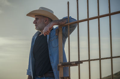 Side view of young woman standing on chainlink fence