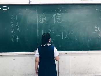 Rear view of girl standing by blackboard in classroom