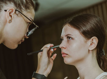 A young makeup artist applies shadows to a girl s eyelids.