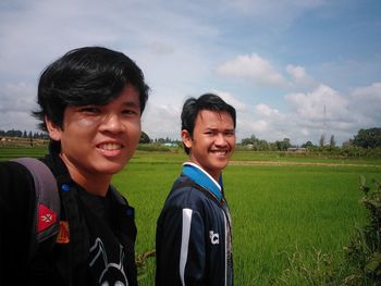 Portrait of smiling young man standing on field against sky