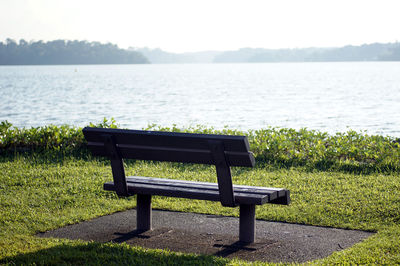 Empty bench by lake in park against sky