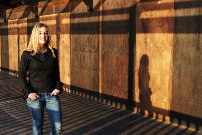 Portrait of blonde woman casting shadow against wooden wall at sunset