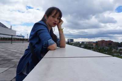 Side view portrait of woman leaning on retaining wall against sky