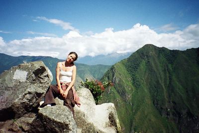 Woman sitting on rock at machu picchu against sky