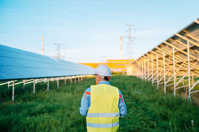 Old construction engineer walking between solar panels on ecological field station