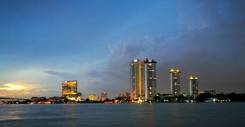 Illuminated cityscape by sea against sky at night