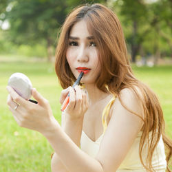Close-up of young woman applying lipstick while sitting outdoors