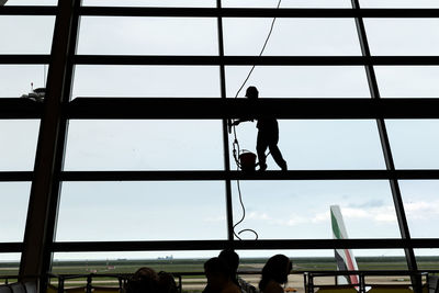 Low angle view of silhouette people on glass window against sky