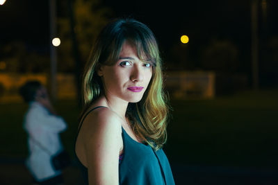 Close-up portrait of young woman standing outdoors at night