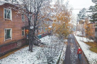 Snow covered road amidst trees and buildings in city