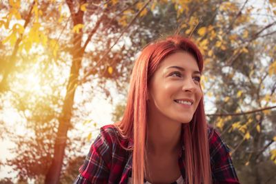 Low angle view of smiling woman looking away against trees during autumn