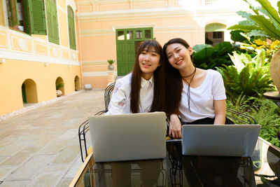 Smiling women with laptop sitting at sidewalk cafe