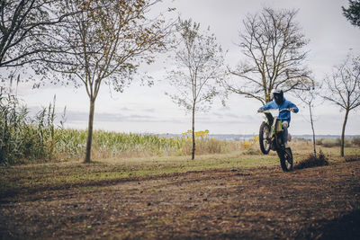 Man riding bicycle on road amidst field against sky