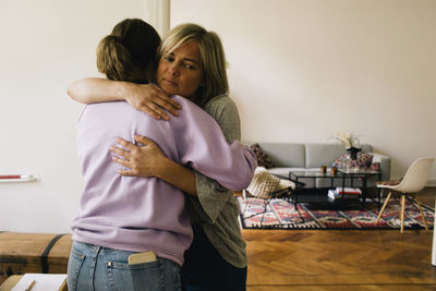 Rear view of girl embracing mother standing at home