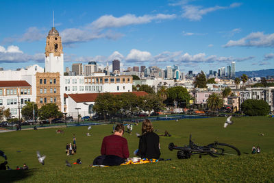 People sitting at park against sky in city