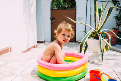 Cute child has fun in inflatable pool with toys in summer in backyard.