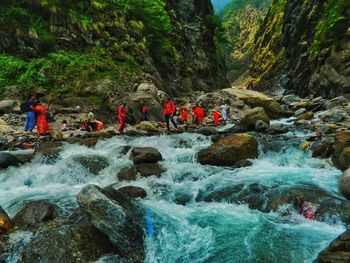 People enjoying on rocks by river against mountain