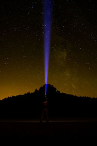 Silhouette man pointing flashlight towards star field in sky at night