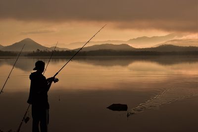 Silhouette person fishing in lake against sky during sunset