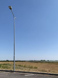 Street amidst field against clear blue sky