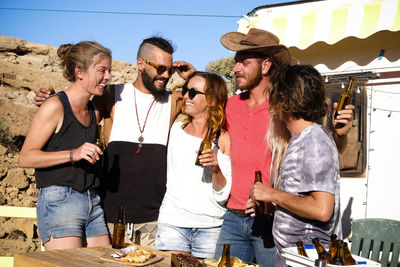 Friends drinking beer while talking against sky