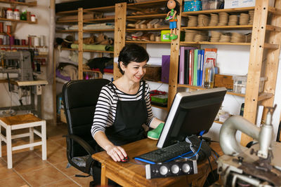 Smiling shoemaker using computer in her workshop