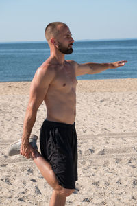 Full length of shirtless man standing at beach against sky