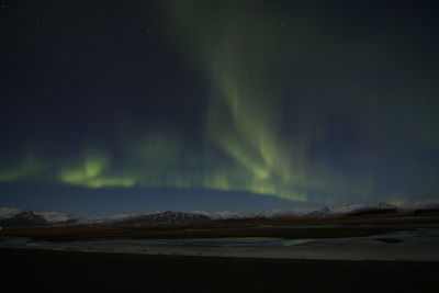 Low angle view of aurora borealis over mountains and lake