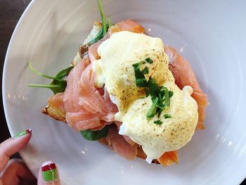 Close-up of cropped hands of woman holding eggs benedict served in plate