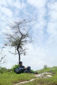 Man sitting on tree against sky