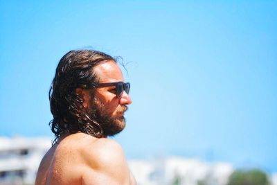 Side view of shirtless man wearing sunglasses against blue sky