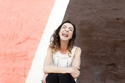 Adult woman sticking her tongue out irreverently in front of a pink and brown wall , san sebastian