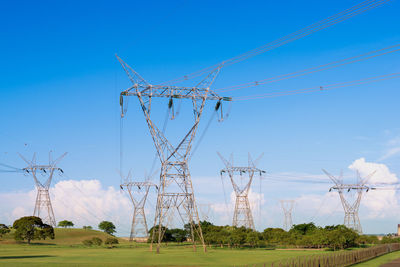 Electricity pylons on field against blue sky