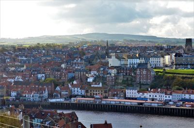 Aerial view of townscape by river against sky