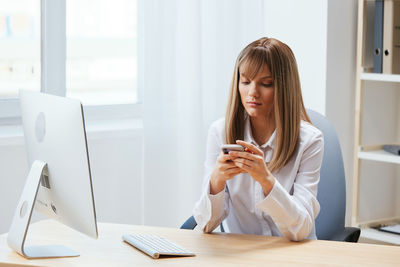 Young woman using mobile phone while sitting on table