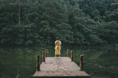Young woman standing on pier over beautiful tranquil lake in green forest