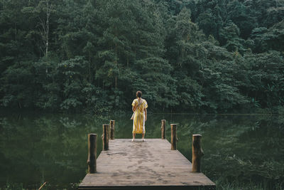 Man standing on pier over lake in forest