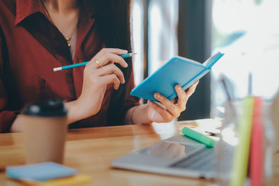 Midsection of woman holding paper with text on table