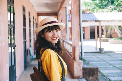 Portrait of smiling young woman standing against built structure