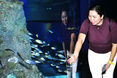 Happy woman touching fish tank glass at aquarium