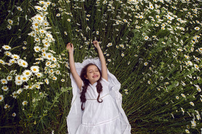 Girl child lies on a camomile field in a white dress in summer