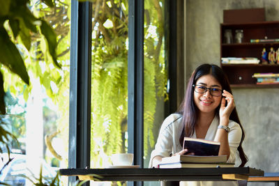 Portrait of young woman using phone while sitting on table
