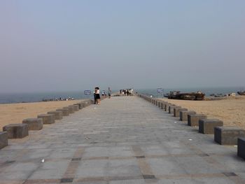 Mid distance view of people on promenade by sea against clear sky