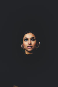 Close-up portrait of young woman against black background