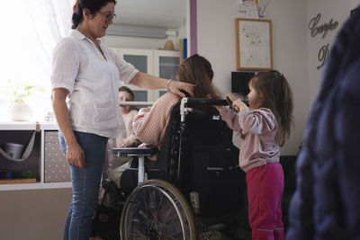 Mother and sister brushing disabled teenage girl's hair in bedroom