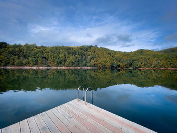 Wooden pontoon on a lake surrounded by forest beginning to change colors in autumn