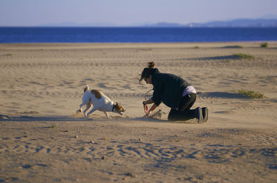 Woman playing with dog at beach against sky