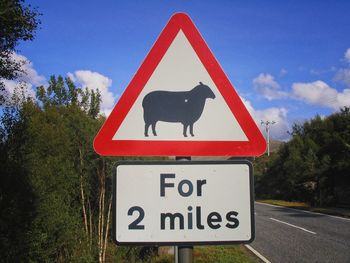 Information sign by road against sky